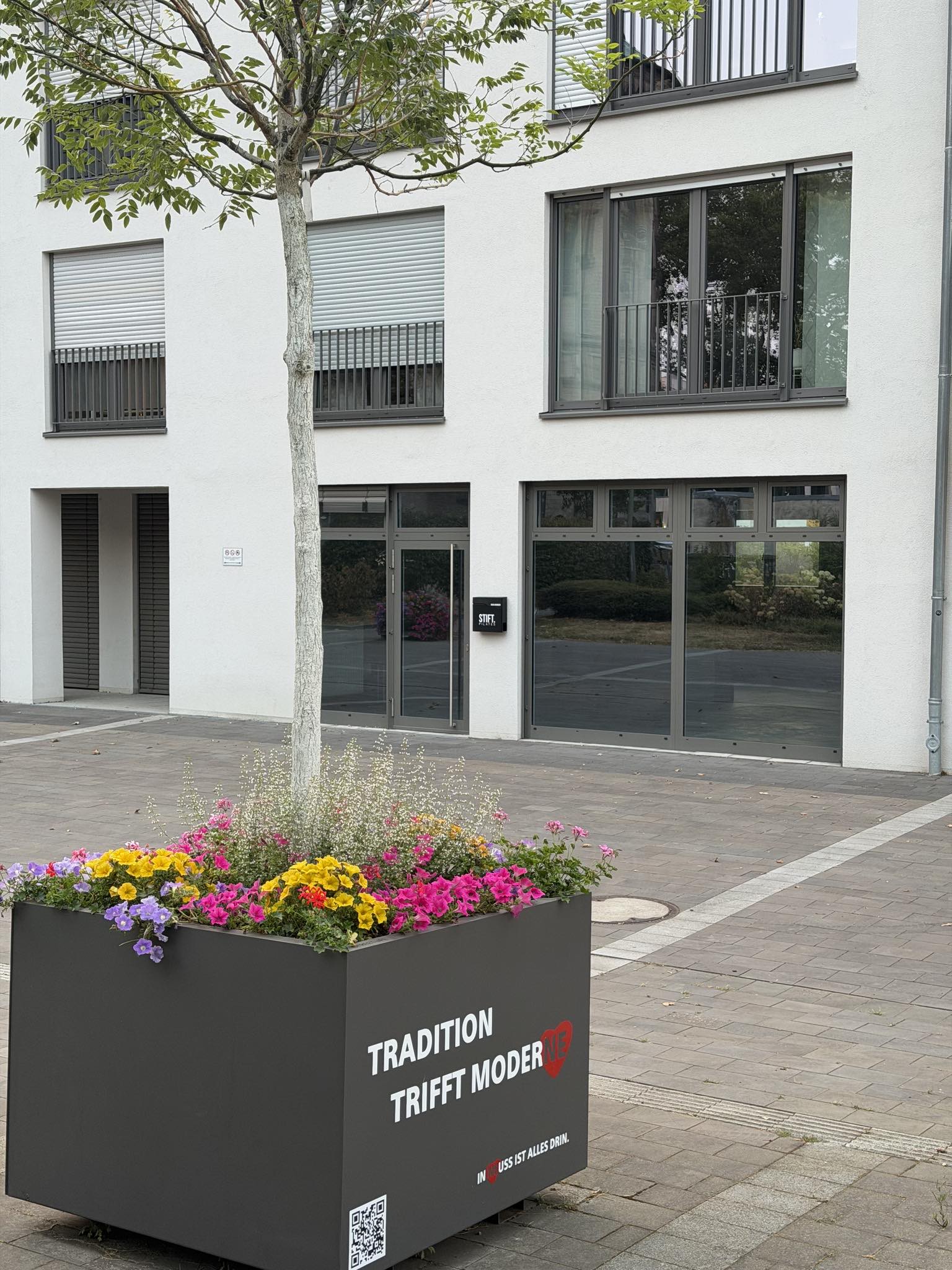Das Studio am Damenstift-Platz in Neuss: Erdgeschoss mit bodentiefer Glasfront, daneben das Schild von STIFT. PILATES
