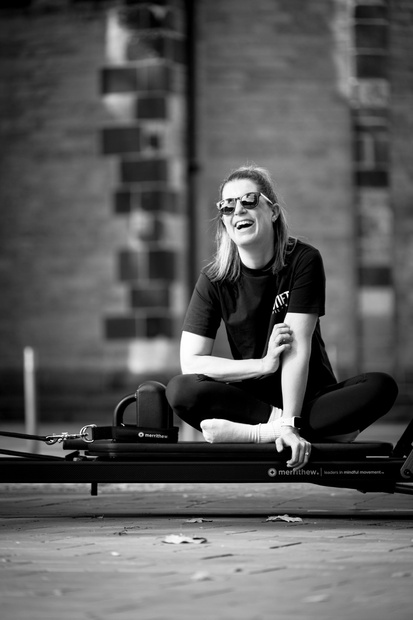 Sara Kremser, Gründerin von STIFT. PILATES, sitzt lachend im Schneidersitz auf einem Reformer