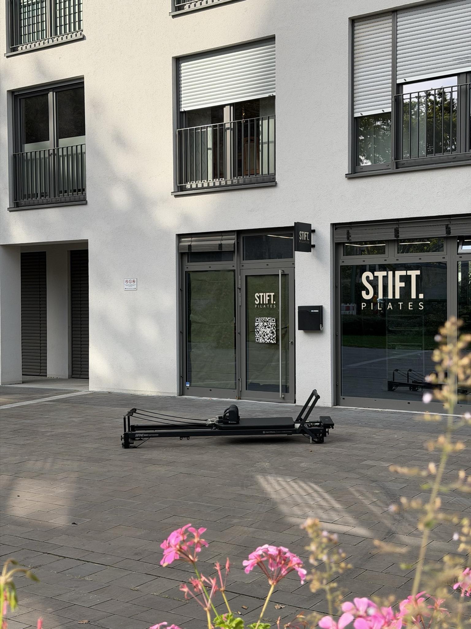 Das Studio am Damenstift-Platz in Neuss: Glasfront mit dem Schriftzug STIFT. PILATES, davor steht ein Reformer auf dem Platz
